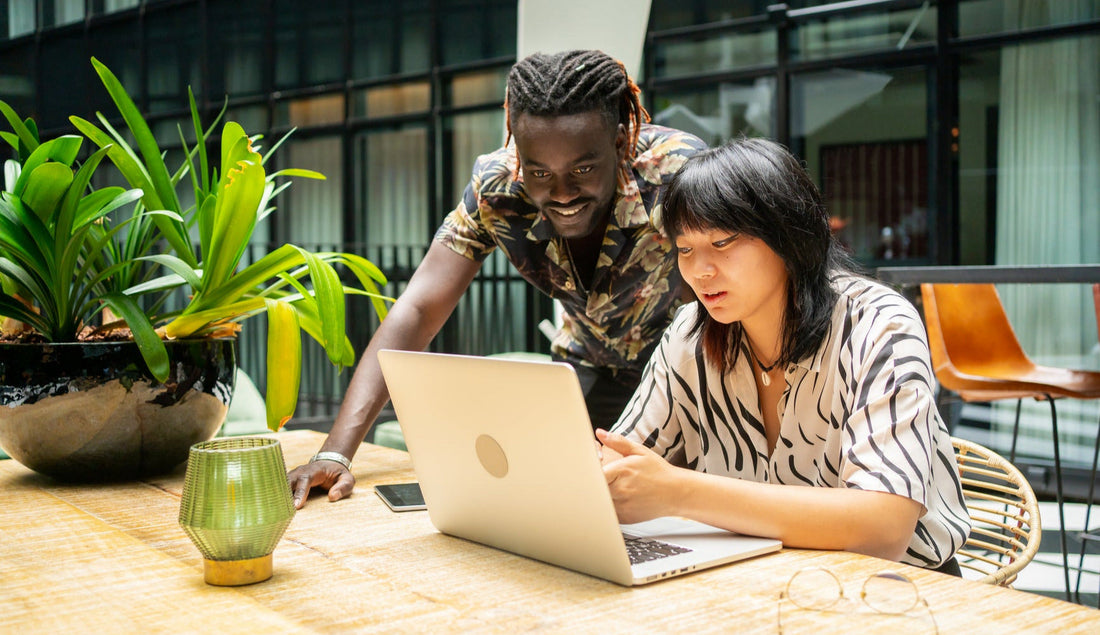 Two people looking at a laptop together in an outdoor setting with plants and furniture.