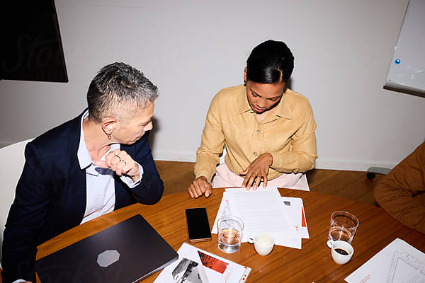 Two people sitting at a table with papers and a laptop, engaged in a discussion.